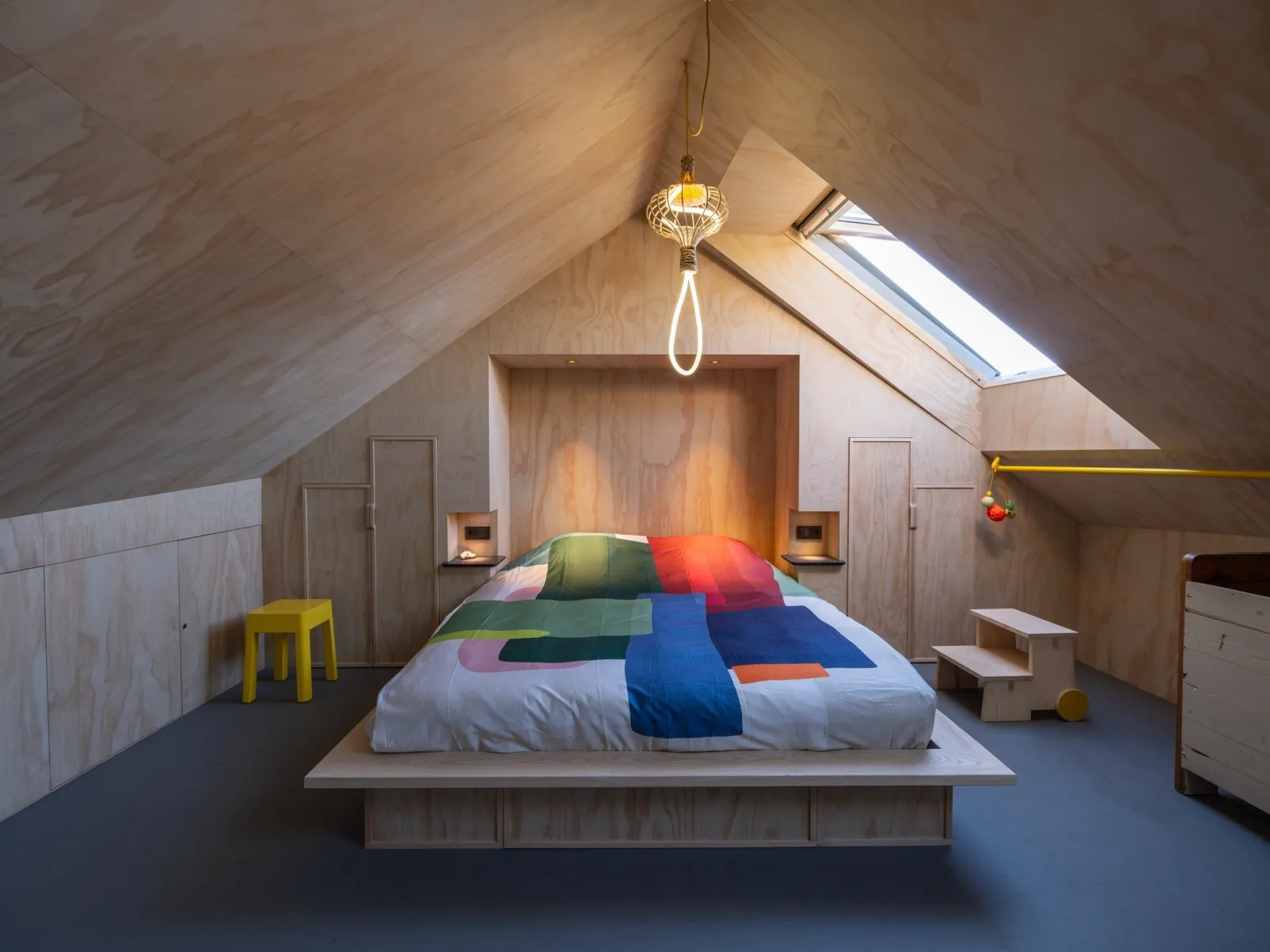Slaapkamer boven met houten wanden, dakraam en een kleurrijk dekbed