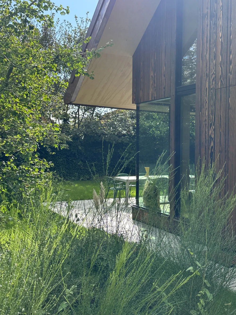 De tuin met wilde grassen en de houten gevel met grote ramen